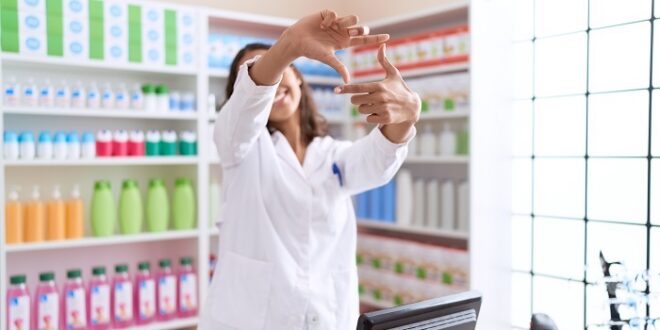 Young african american woman pharmacist smiling confident doing photo gesture with hands at pharmacy